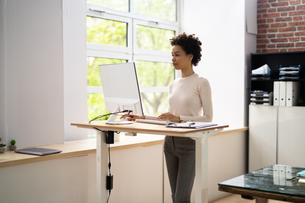 Woman,Using,Adjustable,Height,Standing,Desk,In,Office,For,Good - welltica.dk - Vejen til et bedre liv