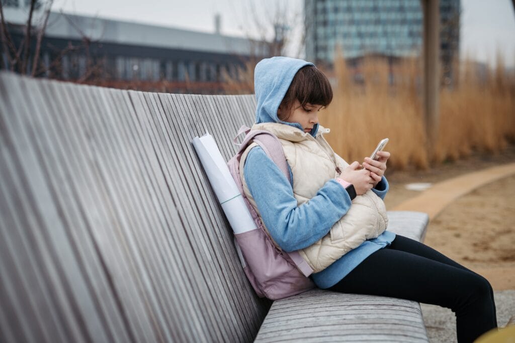Girl,Standing,In,Front,Of,School,Building,,Scrolling,On,Smartphone. - welltica.dk - Vejen til et bedre liv