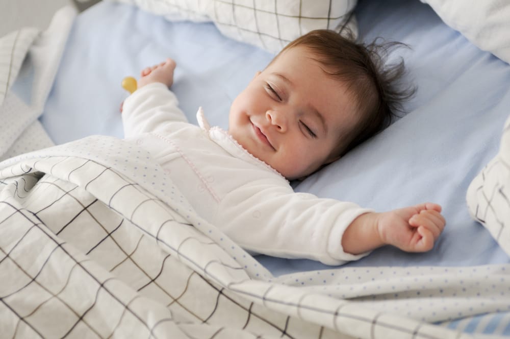 Smiling,Baby,Girl,Lying,On,A,Bed,Sleeping,On,Blue - welltica.dk - Vejen til et bedre liv