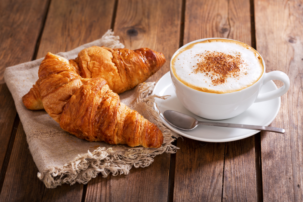 CupOfCappuccinoCoffeeWithCroissantsOnWoodenTable - welltica.dk - Vejen til et bedre liv