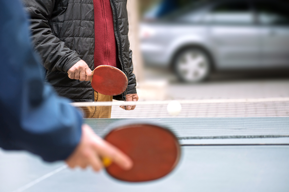 HappyMatureManAndHisSonPlayingTableTennisOutdoor - welltica.dk - Vejen til et bedre liv