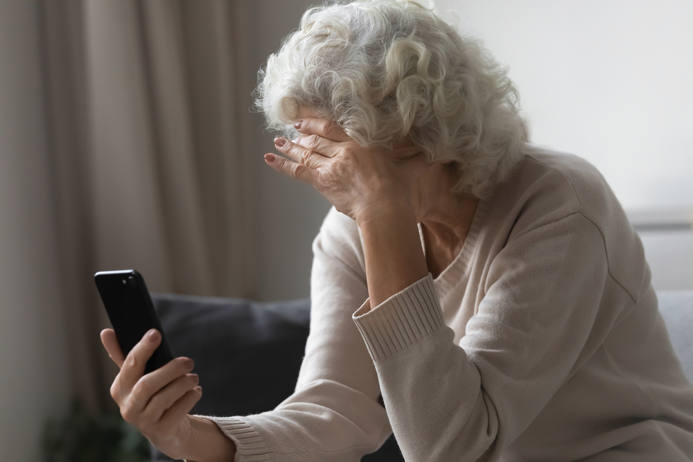 SadSeniorLadyUsingMobilePhoneAtHomeSittingOn - welltica.dk - Vejen til et bedre liv