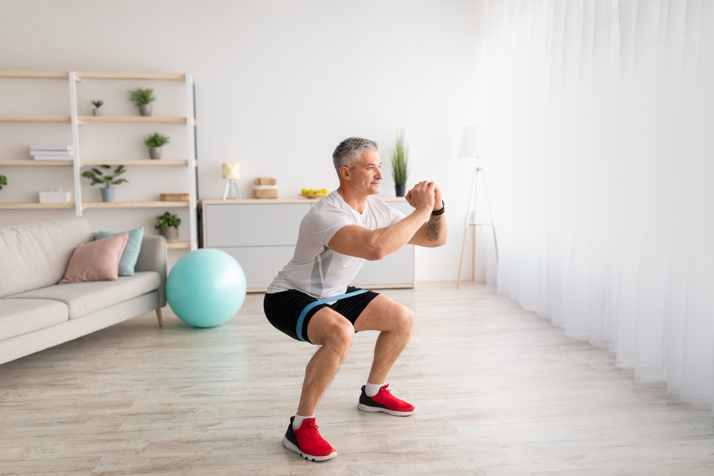MorningTrainingSportyMatureManDoingSquatsExercisingInLiving - welltica.dk - Vejen til et bedre liv