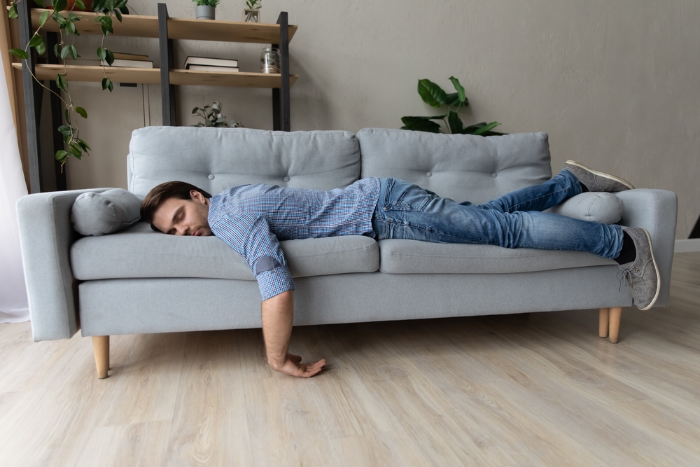 ExhaustedYoungManFellAsleepOnComfortableCouchInModern - welltica.dk - Vejen til et bedre liv