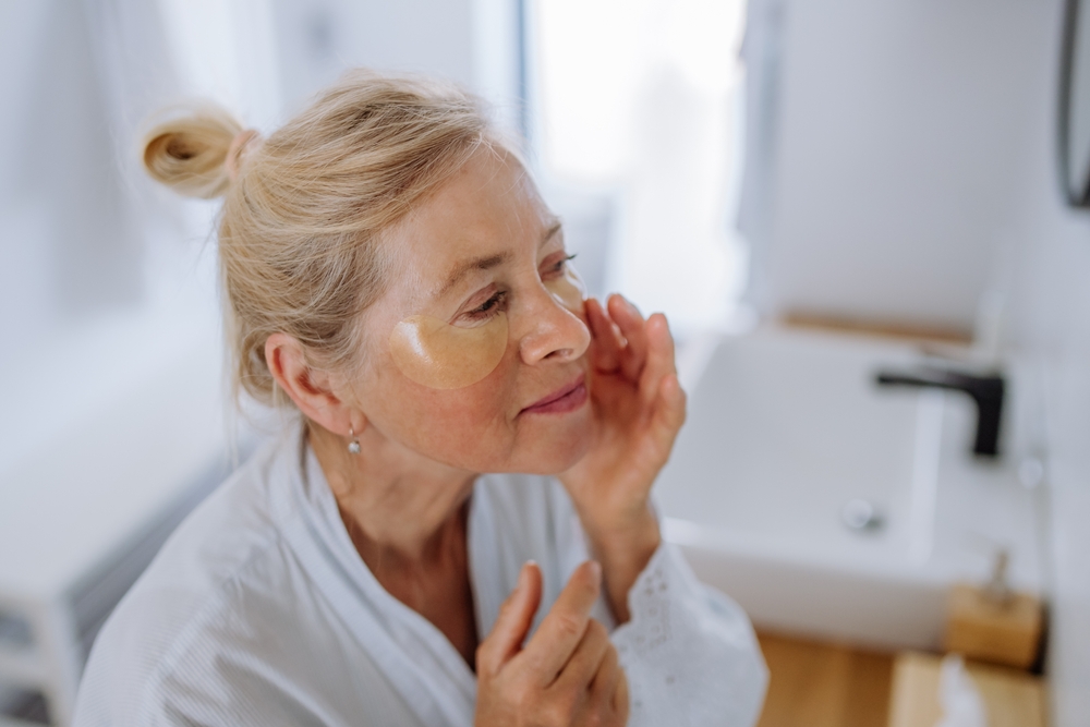 BeautifulSeniorWomanInBathrobeApplyingEyePatchesForPuffiness - welltica.dk - Vejen til et bedre liv