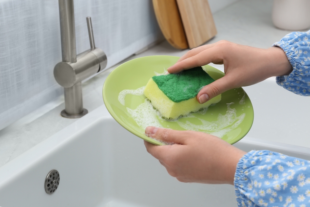 WomanWashingPlateAboveSinkInKitchenCloseup - welltica.dk - Vejen til et bedre liv