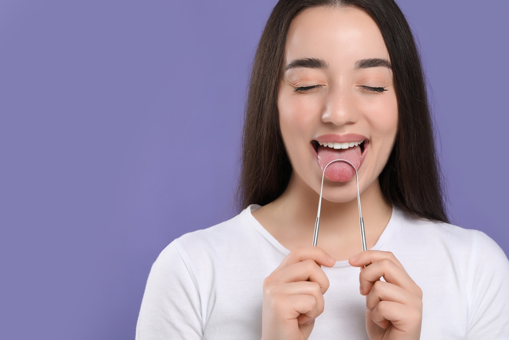 HappyWomanBrushingHerTongueWithCleanerOnVioletBackground - welltica.dk - Vejen til et bedre liv