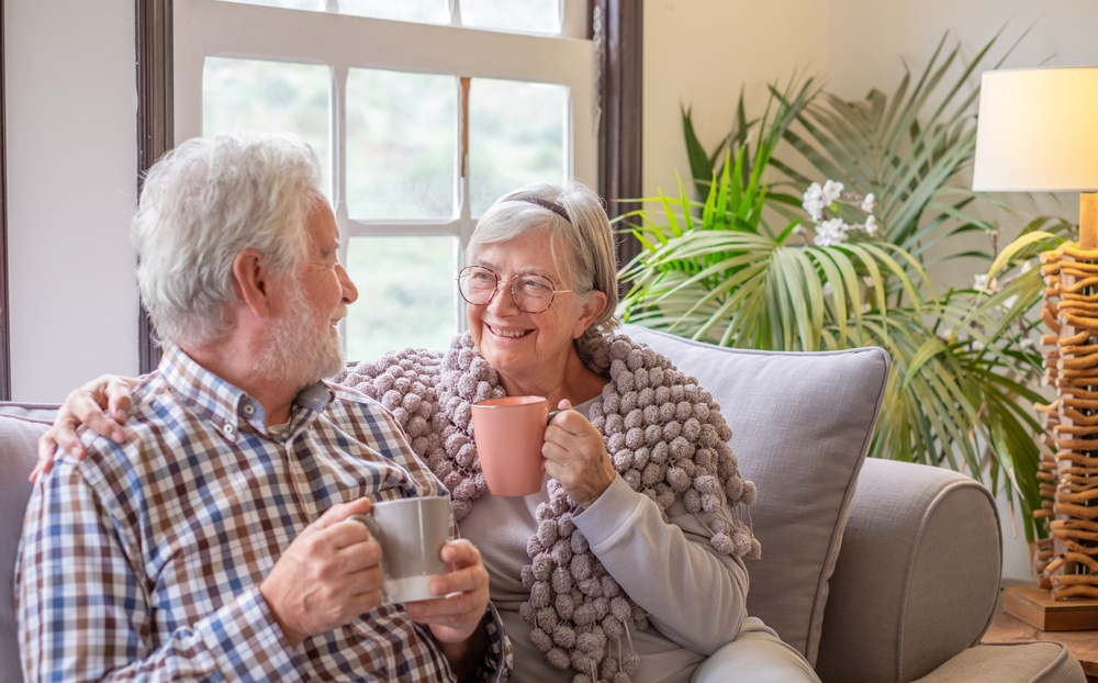 Happy70sWhiteHairedSeniorCoupleSittingOnSofaIn - welltica.dk - Vejen til et bedre liv