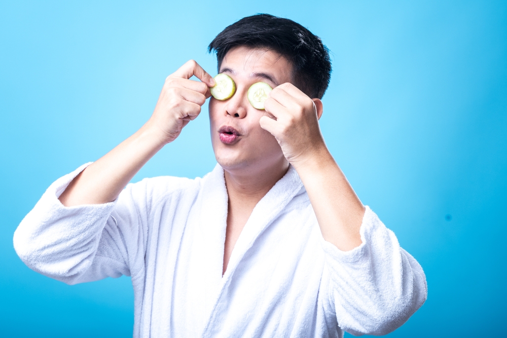 AsianManInAWhiteBathrobePlayfullyHoldsCucumberSlices - welltica.dk - Vejen til et bedre liv