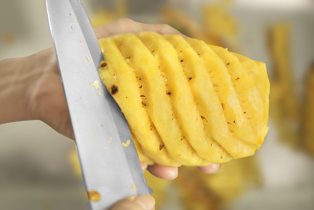 SlicingPineappleUsingSilverKnifeByHandOverSlicedOut - welltica.dk - Vejen til et bedre liv