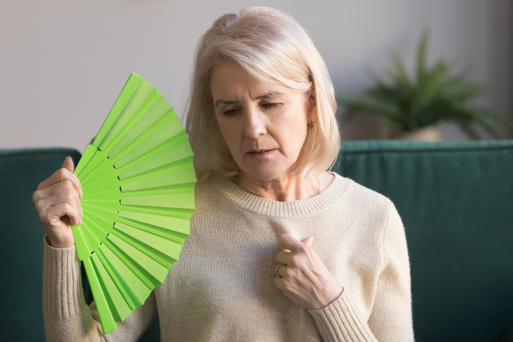 OverheatedElderlyWomanSittingOnCouchWavingGreenFanTo - welltica.dk - Vejen til et bedre liv