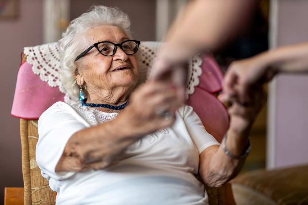 FemaleHomeCarerSupportingOldWomanToStandUpFrom - welltica.dk - Vejen til et bedre liv