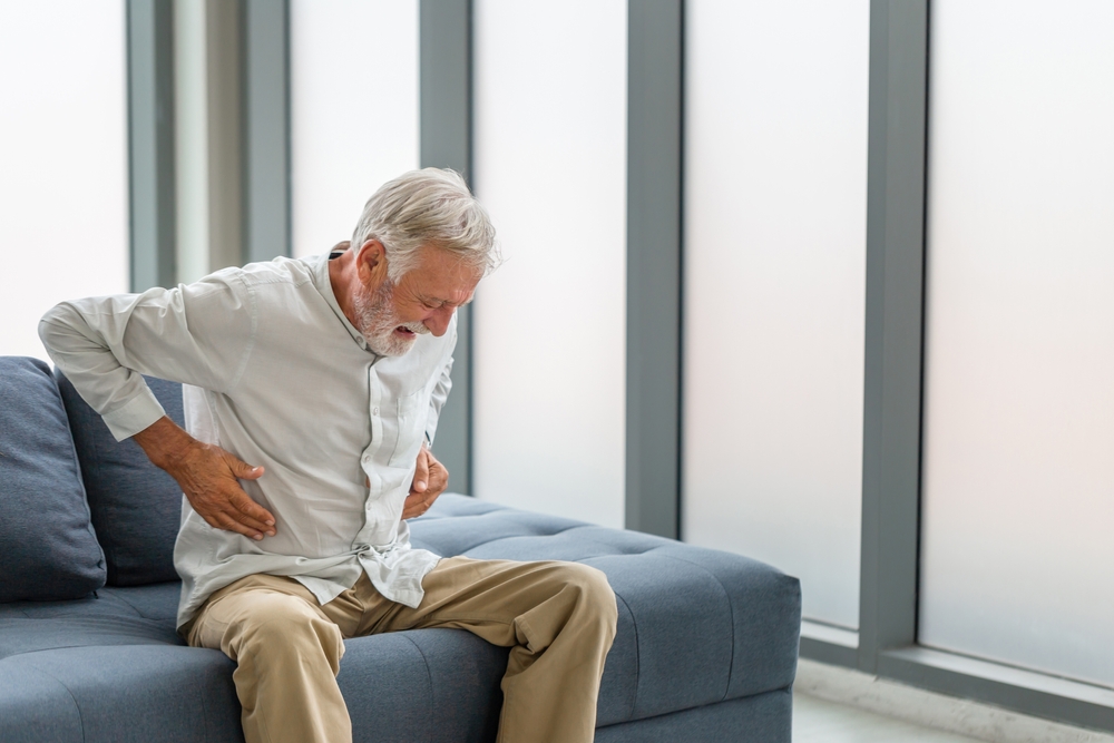SeniorManSufferingStomachAcheSittingOnACouchIn - welltica.dk - Vejen til et bedre liv