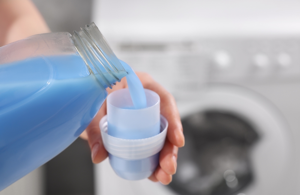 WomanPouringFabricSoftenerFromBottleIntoCapForWashing - welltica.dk - Vejen til et bedre liv