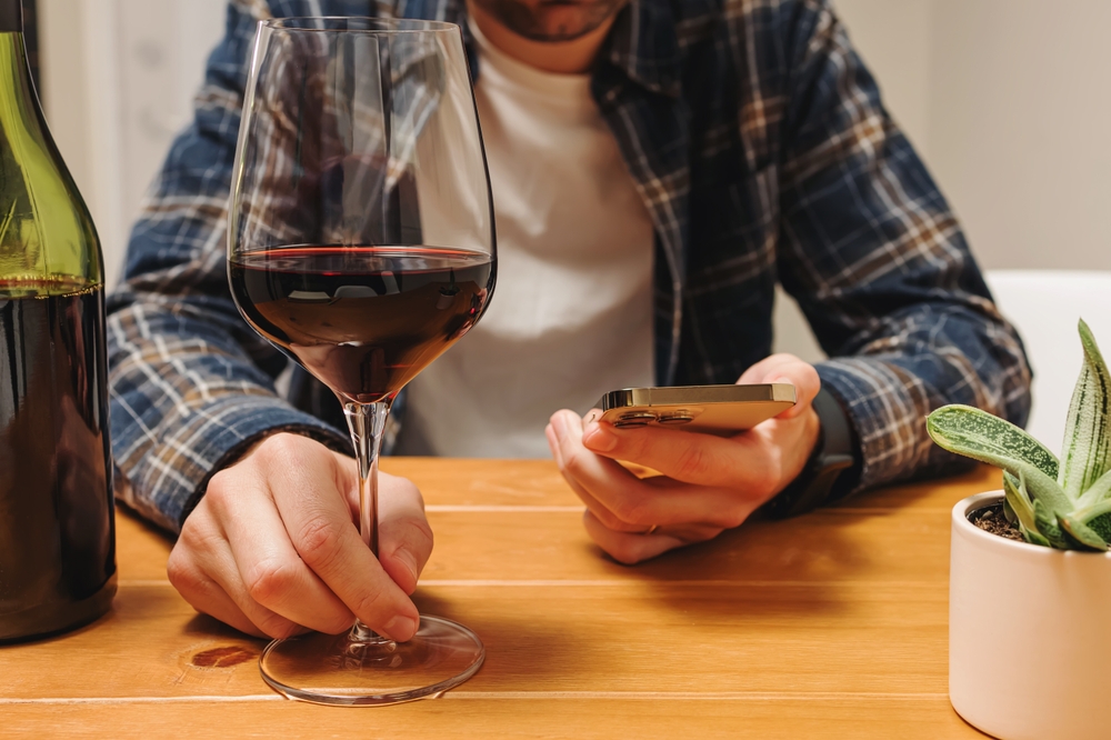 UnrecognizableManHoldingAPhoneAndAGlassOfWine - welltica.dk - Vejen til et bedre liv