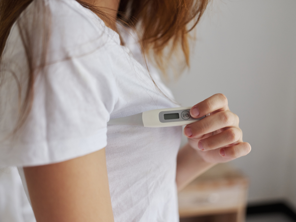 WomanHoldingAThermometerUnderHerArmBehindAWhite - welltica.dk - Vejen til et bedre liv