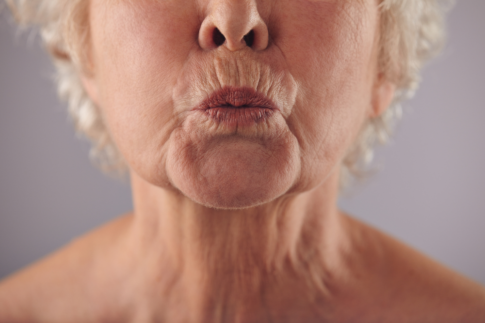 Close-upPortraitOfMatureWomanPuckeringLipsAgainstGreyBackground - welltica.dk - Vejen til et bedre liv