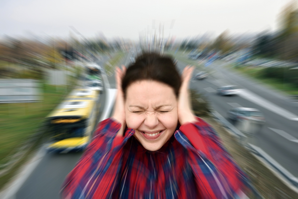 WomanWithClosedEyesCoveringHerEarsInTheStreet - welltica.dk - Vejen til et bedre liv