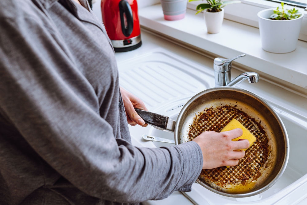 WomansHandWashesBurntGreasyFryingPanWithKitchenWashcloth - welltica.dk - Vejen til et bedre liv