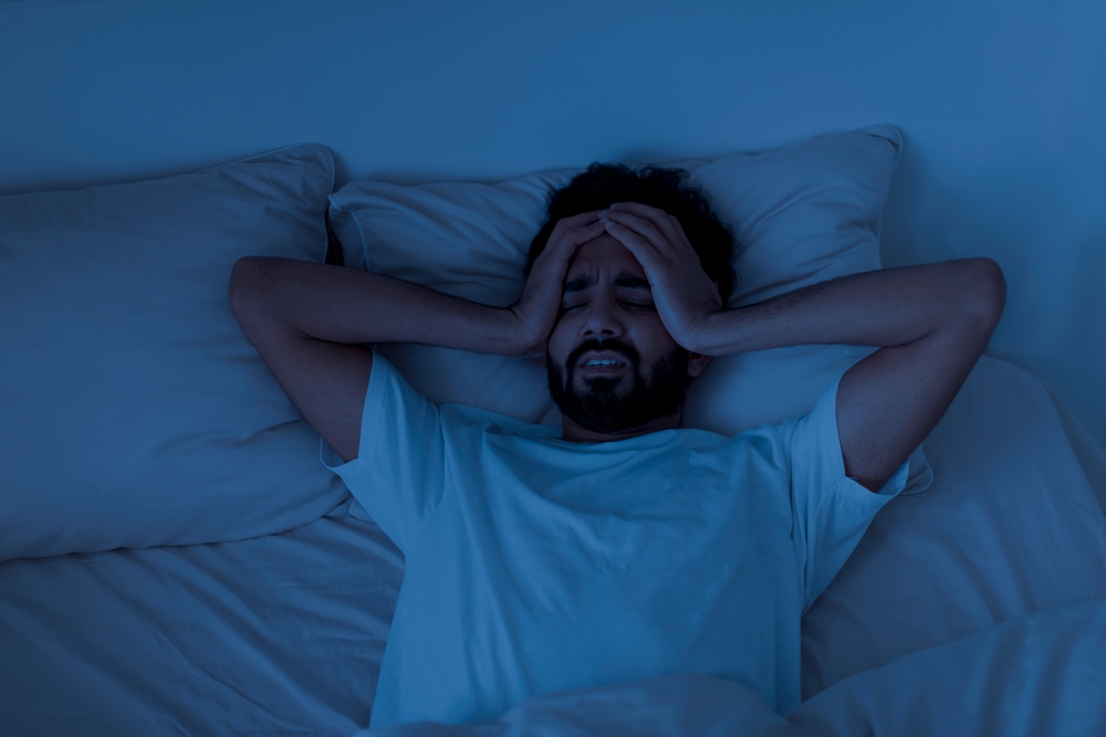 SleepingProblemStressedYoungIndianManLyingAloneInBed - welltica.dk - Vejen til et bedre liv