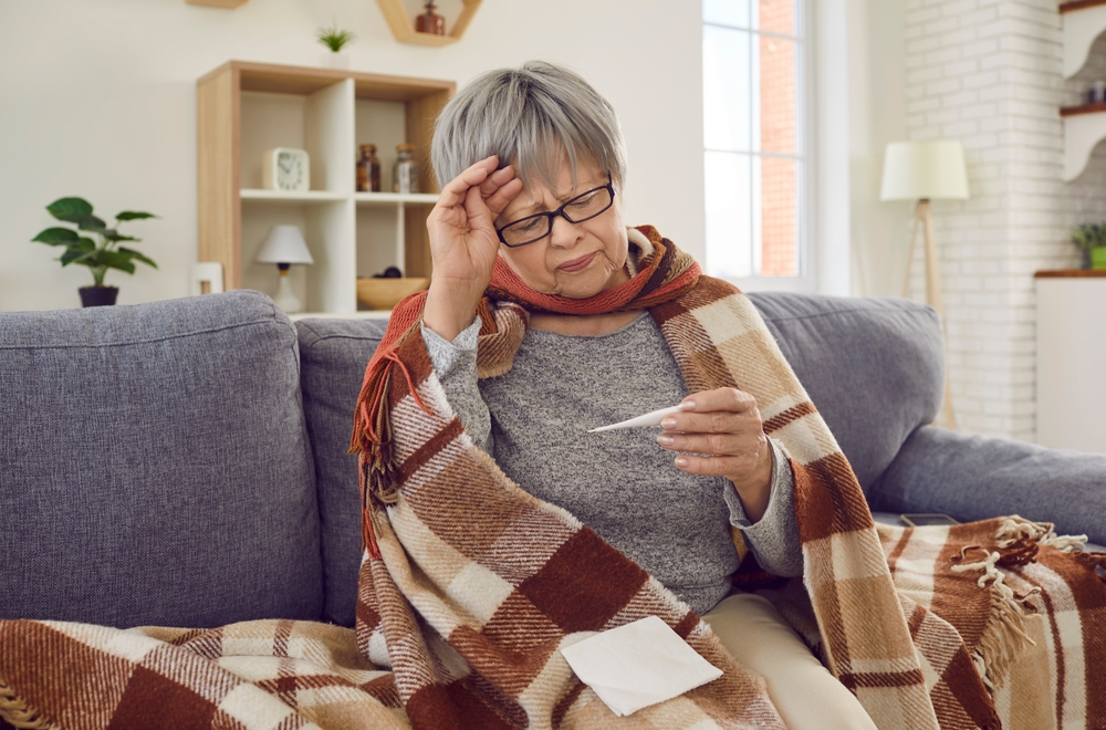 SickSeniorWomanCheckingHerTemperatureWrappedInABlanket - welltica.dk - Vejen til et bedre liv