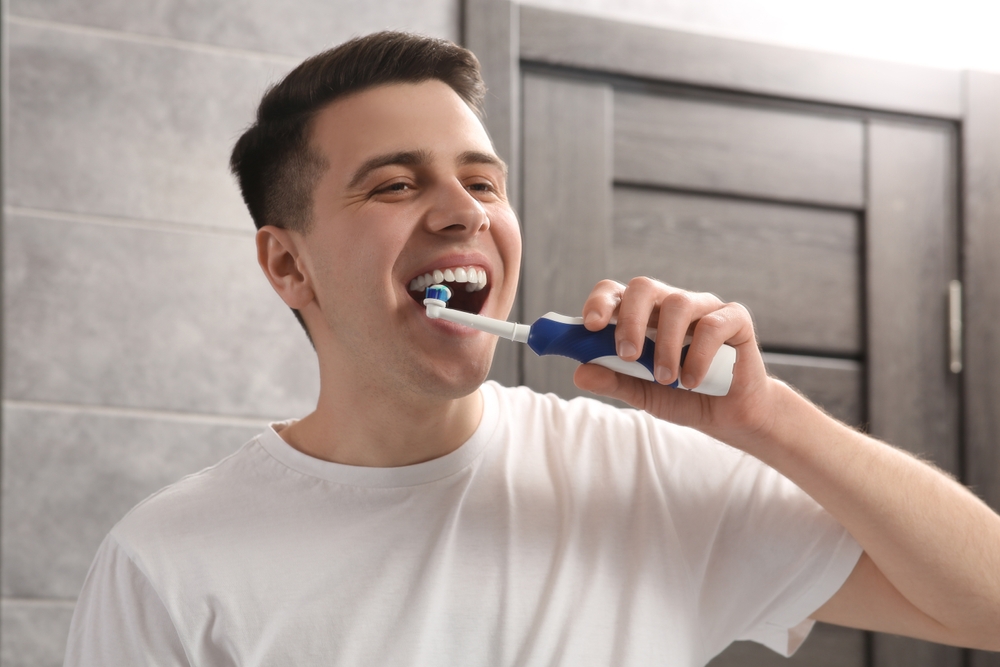 ManBrushingHisTeethWithElectricToothbrushInBathroom - welltica.dk - Vejen til et bedre liv