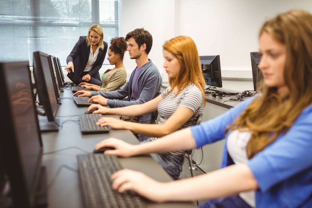 ComputerTeacherHelpingAPrettyStudentInHerClassAt - welltica.dk - Vejen til et bedre liv