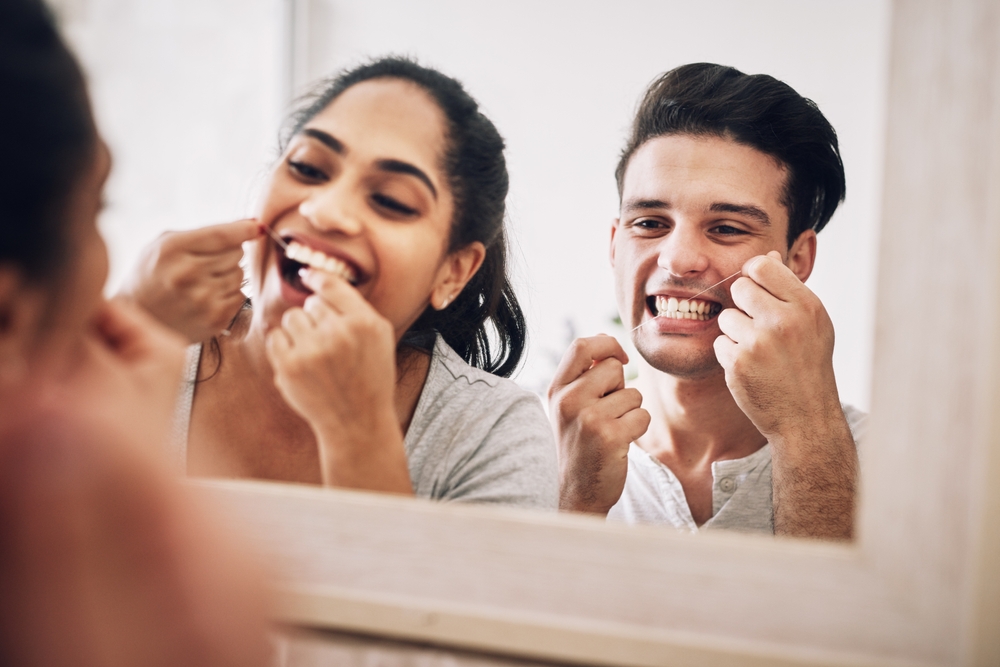 CoupleDentalFlossAndMirrorInBathroomHomeAndTogether - welltica.dk - Vejen til et bedre liv