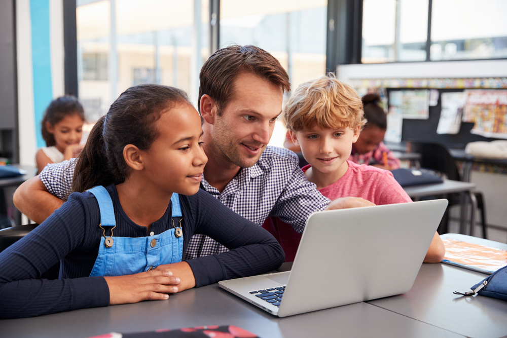 TeacherAndTwoYoungStudentsUseLaptopComputerInClass - welltica.dk - Vejen til et bedre liv