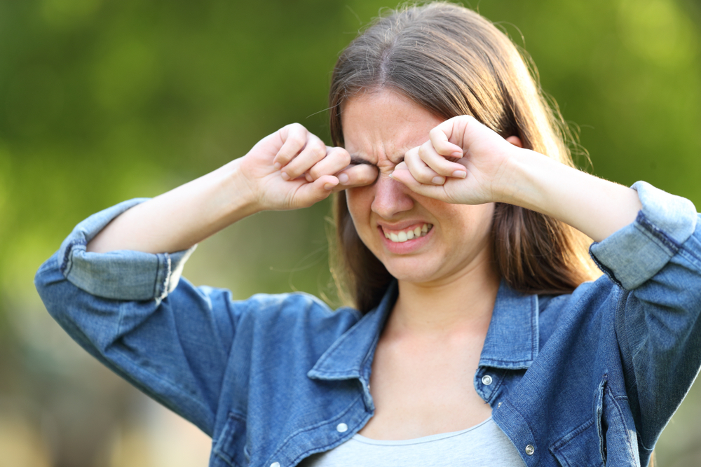 WomanSufferingItchingScratchingEyesOutdoorsInAPark - welltica.dk - Vejen til et bedre liv