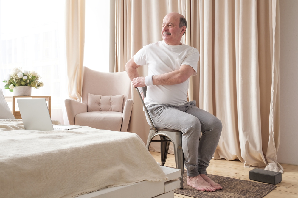 SportySeniorManPracticingYogaUsingChairDoingParivrttaUtkatasana - welltica.dk - Vejen til et bedre liv