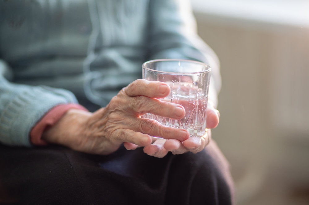 AnElderlyWomanHoldsAGlassGlassWithWaterIn - welltica.dk - Vejen til et bedre liv