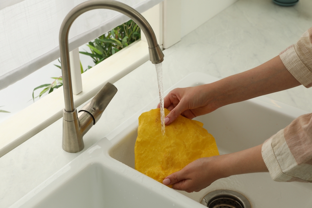WomanWashingBeeswaxFoodWrapUnderTapWaterInKitchen - welltica.dk - Vejen til et bedre liv