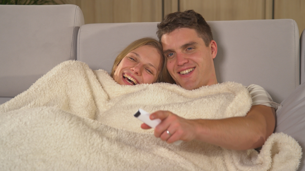 CloseUpCuteCoupleSnugglingUnderBlanketOnACouch - welltica.dk - Vejen til et bedre liv