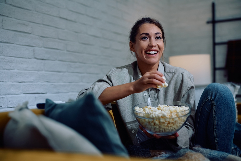 HappyWomanWatchingMovieAndEatingPopcornWhileRelaxingIn - welltica.dk - Vejen til et bedre liv
