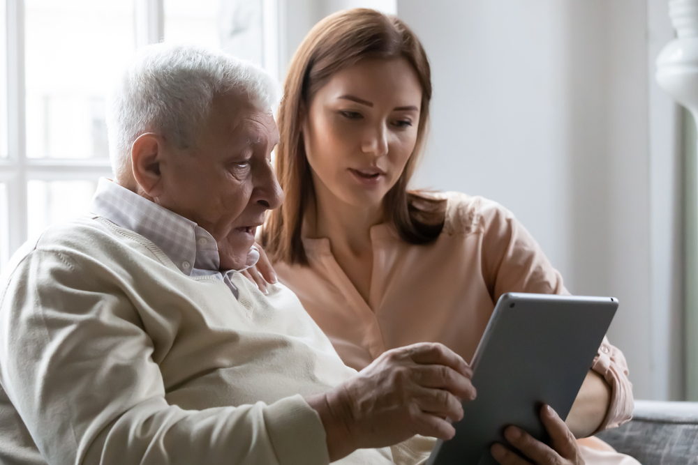 CaringGrownupDaughterTeachingOlderFatherToUseComputerTablet - welltica.dk - Vejen til et bedre liv