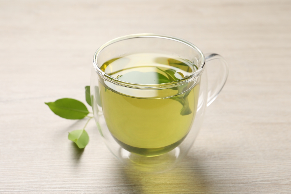 RefreshingGreenTeaInCupAndLeavesOnWoodenTable - welltica.dk - Vejen til et bedre liv