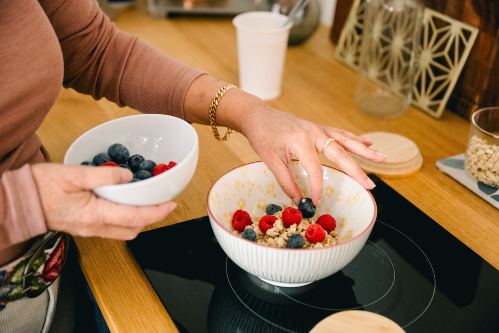 ElderlyWomanPreparingOatmealWithBerriesForBreakfastInKitchen - welltica.dk - Vejen til et bedre liv