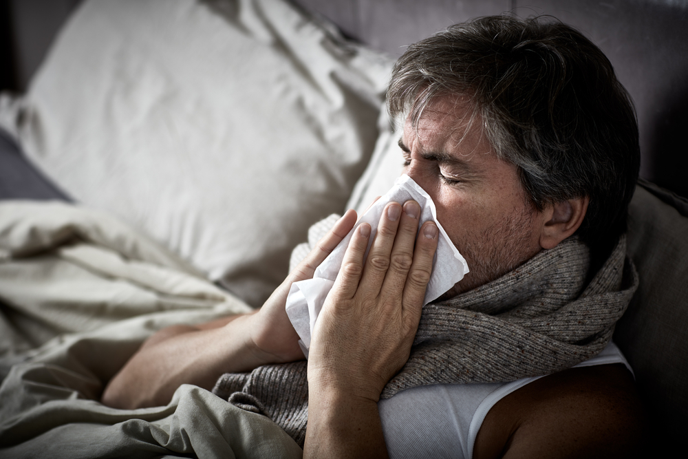 SickManWithColdLyingInBedAndBlowNose - welltica.dk - Vejen til et bedre liv