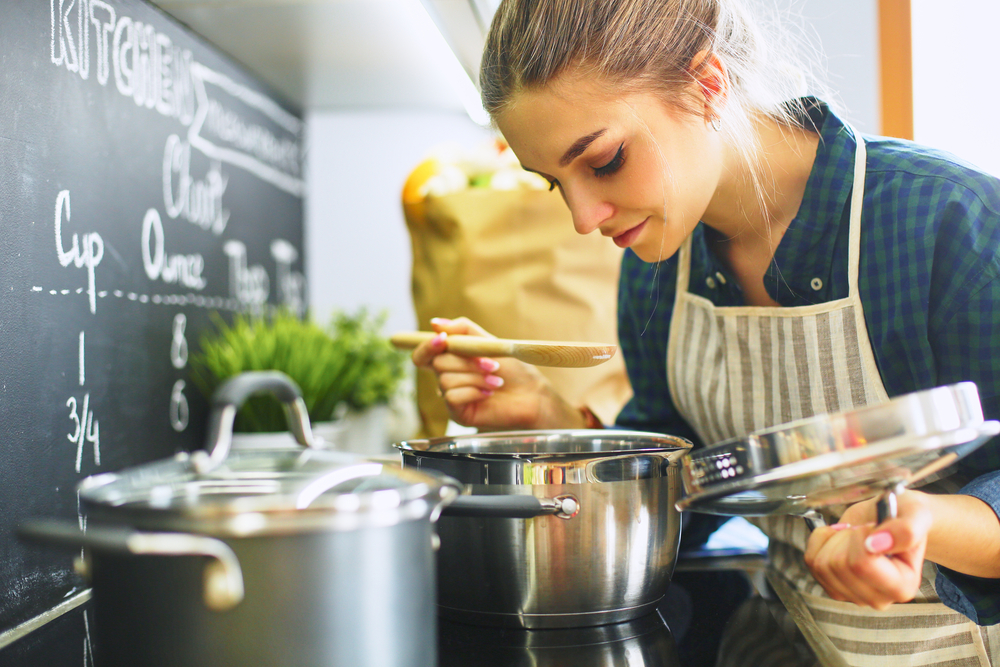 YoungWomanCookingInHerKitchenStandingNearStove - welltica.dk - Vejen til et bedre liv
