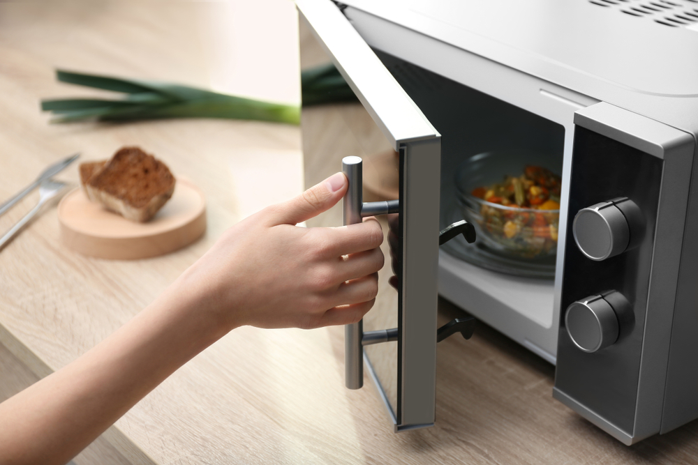 YoungWomanUsingMicrowaveOvenOnTableInKitchen - welltica.dk - Vejen til et bedre liv