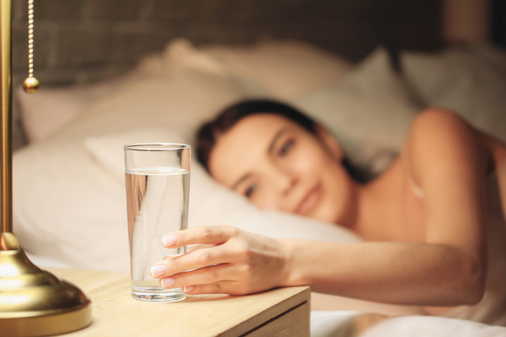 BeautifulYoungWomanTakingGlassOfWaterFromBedsideTable - welltica.dk - Vejen til et bedre liv