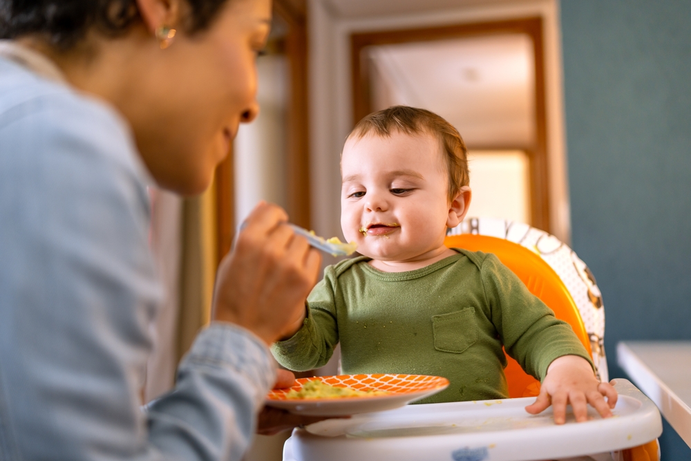 JoyfulBabyBoyInGreenOutfitBeingSpoon-fedByLoving - welltica.dk - Vejen til et bedre liv